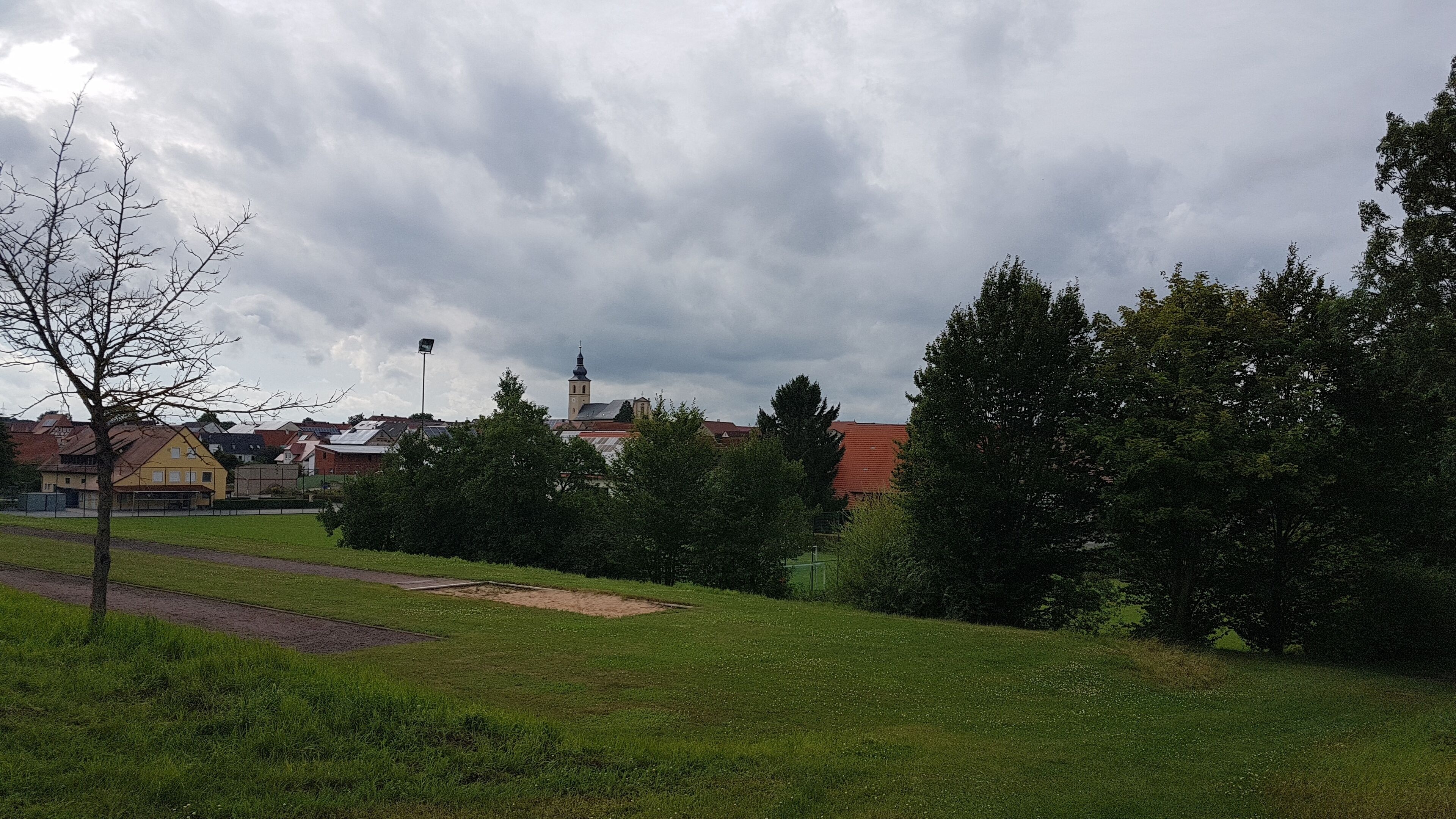 A grassy field with a church and residential buildings in the background.