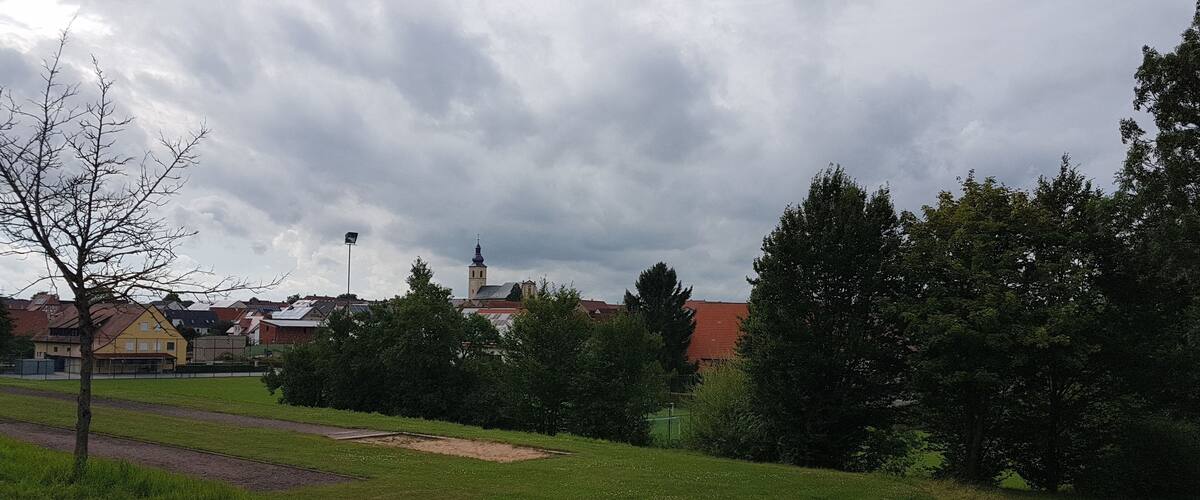 A grassy field with a church and residential buildings in the background.