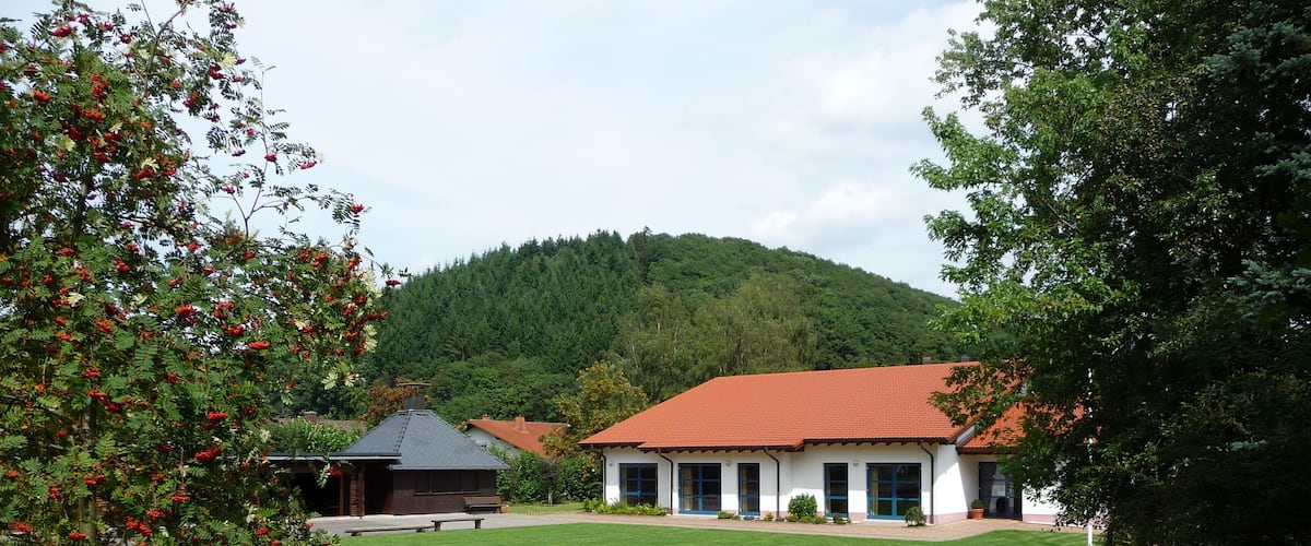 A green lawn, a building with a red roof, and a forested hill in the background.