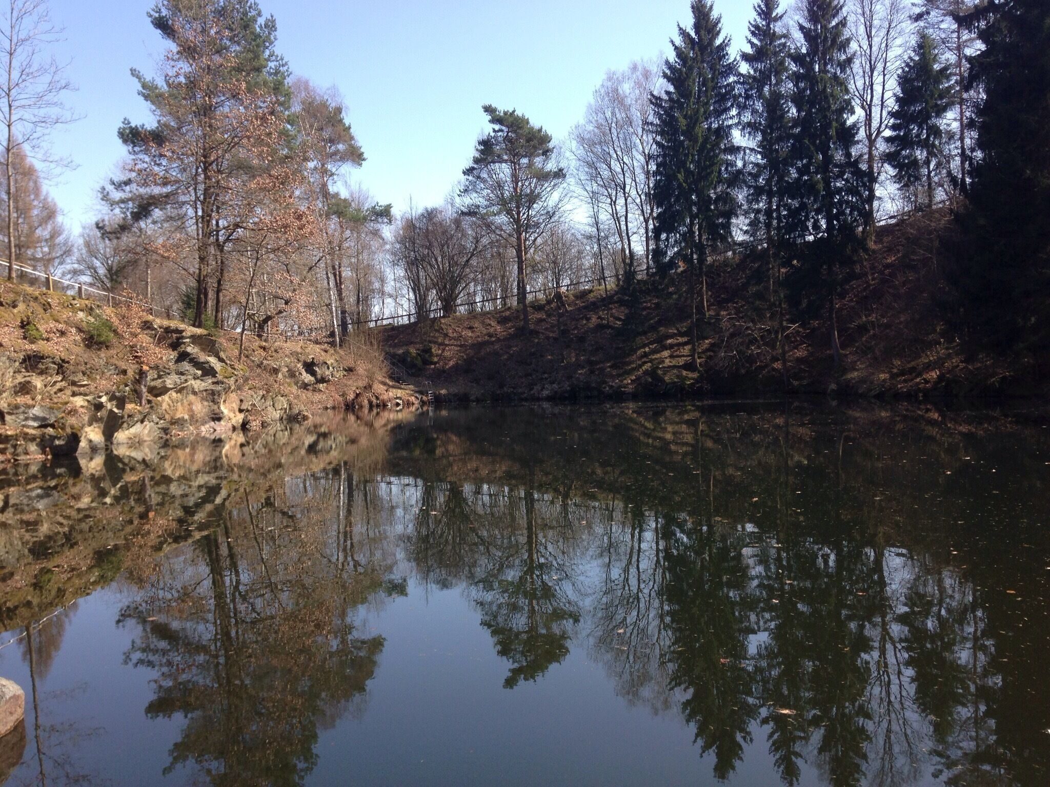 A calm river reflecting trees and a rocky bank.