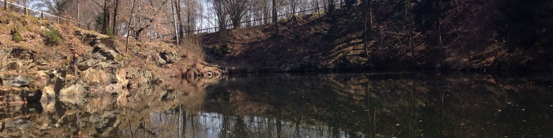 A calm river reflecting trees and a rocky bank.