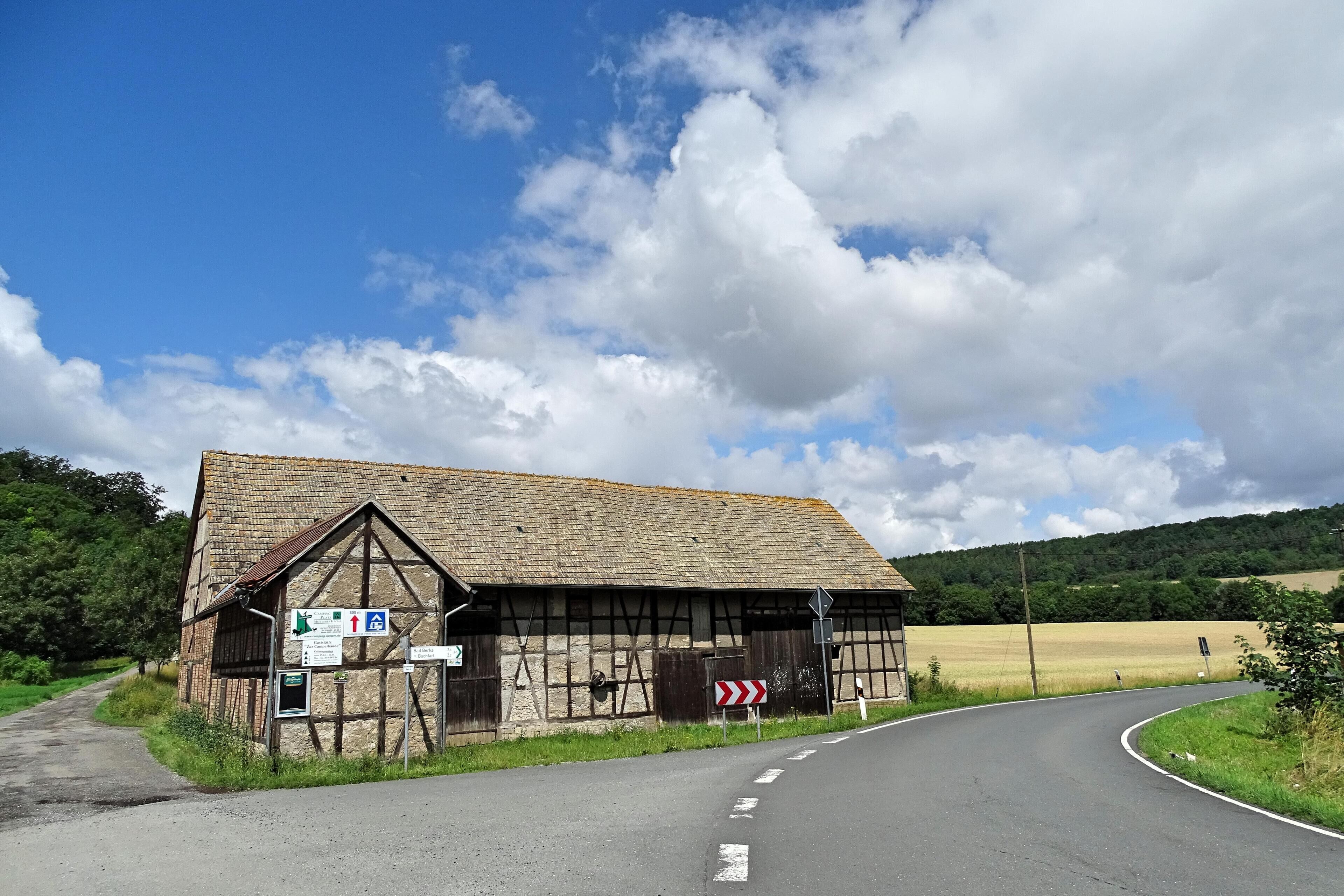 A rural road curving around a traditional half-timbered building with directional signs.