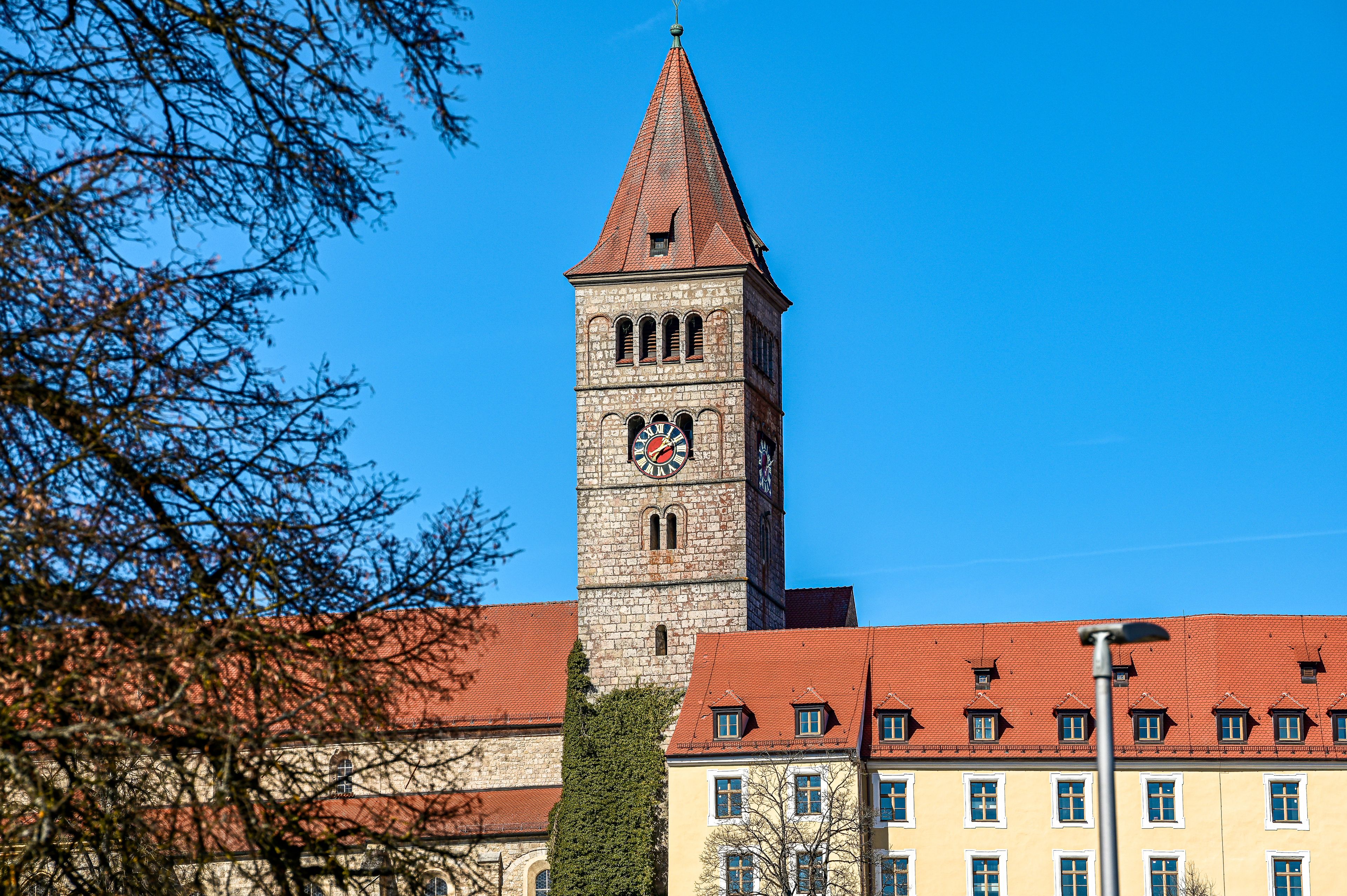 A historic tower with a clock, surrounded by buildings with red-tiled roofs.