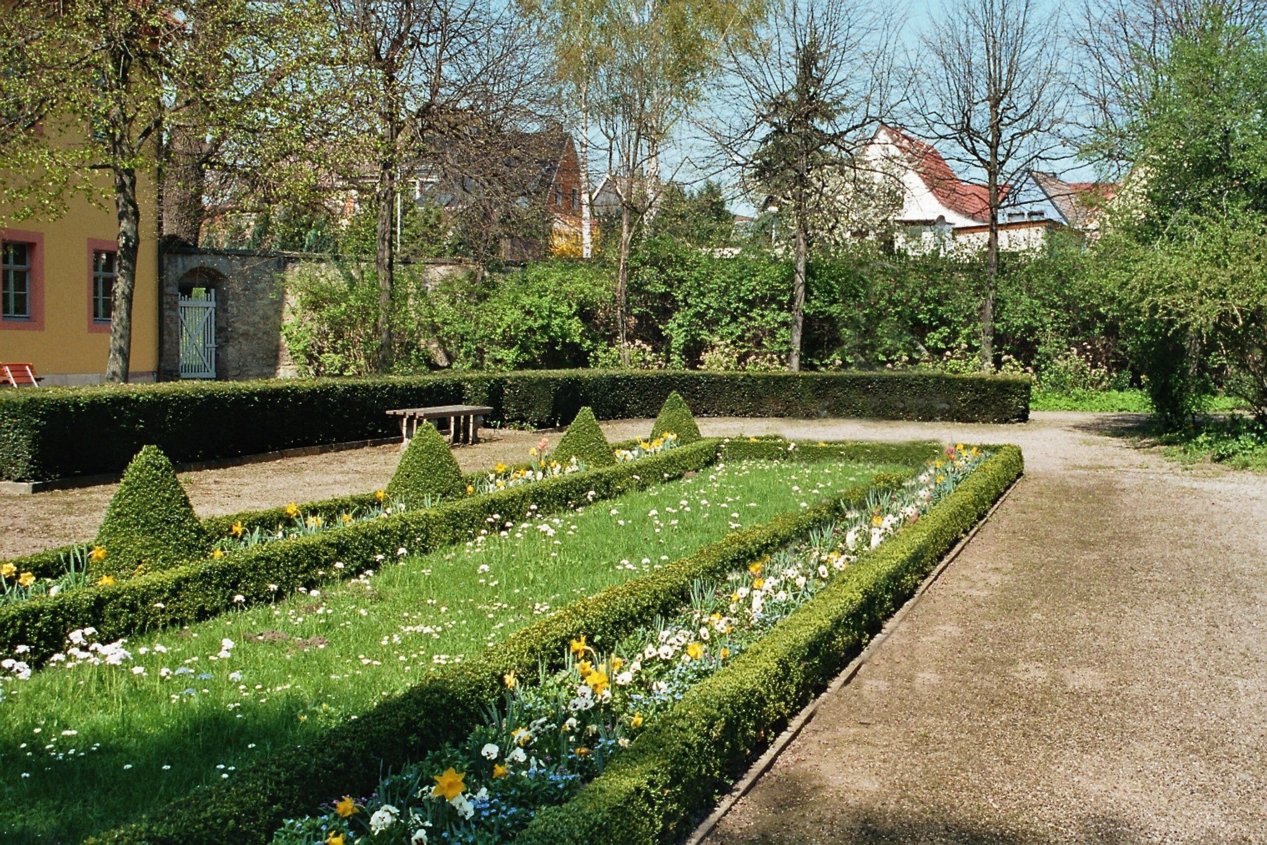 A formal garden with neatly trimmed hedges, flower beds, and a pathway.