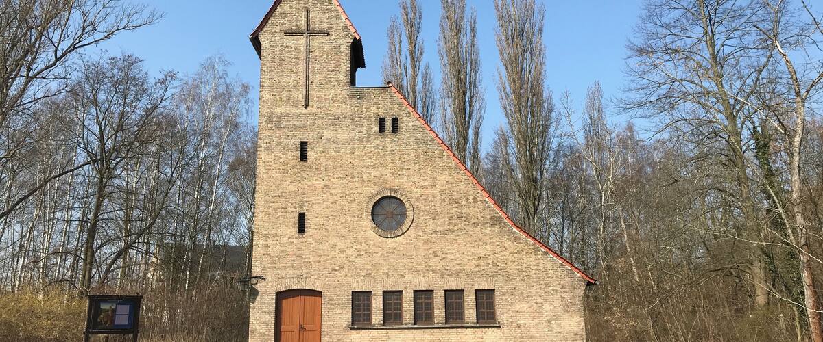 A small brick church with a cross on the tower, surrounded by trees.