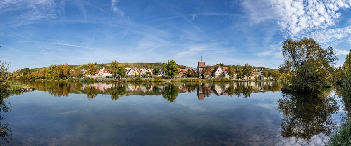 A calm lake reflecting houses and trees, with a clear sky above.
