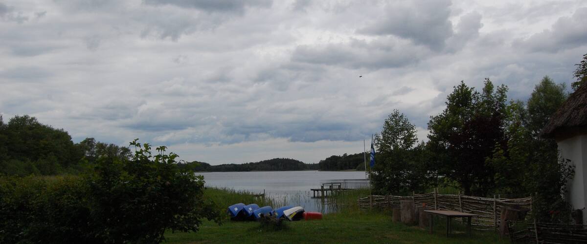 A lakeside campsite with tents, a dock, and a thatched-roof building.