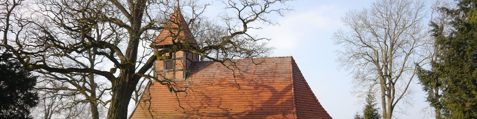 A stone church with a red-tiled roof and a bell tower, surrounded by trees and a well-maintained lawn.
