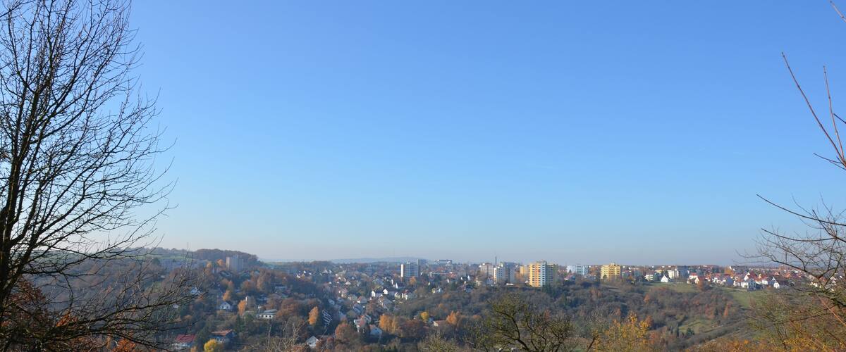 A hilly landscape with autumn-colored trees, a town in the valley, and a clear blue sky.