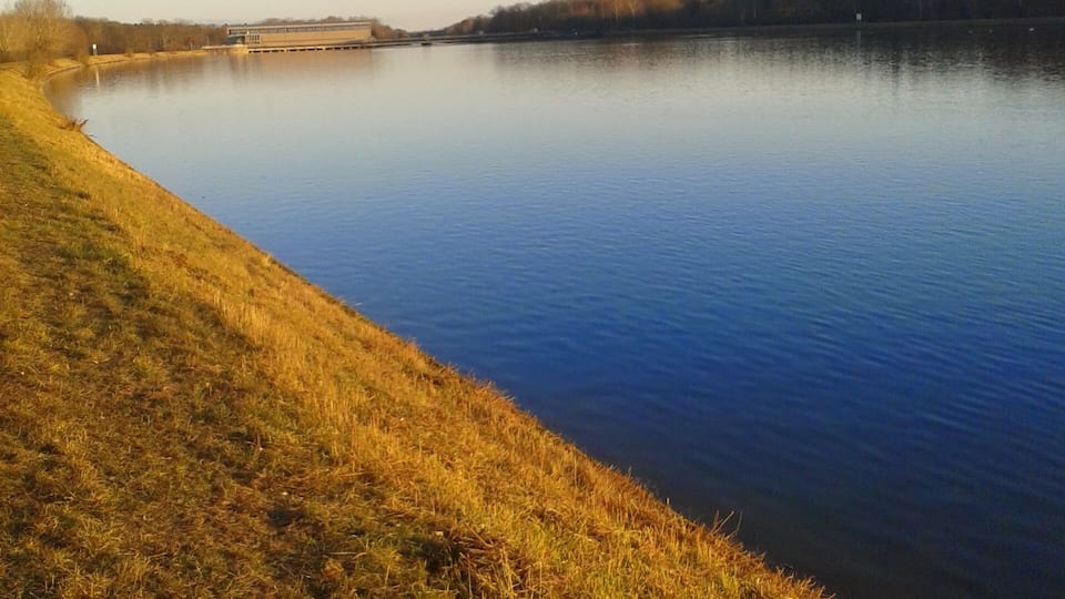 A calm river with grassy banks and a distant building.