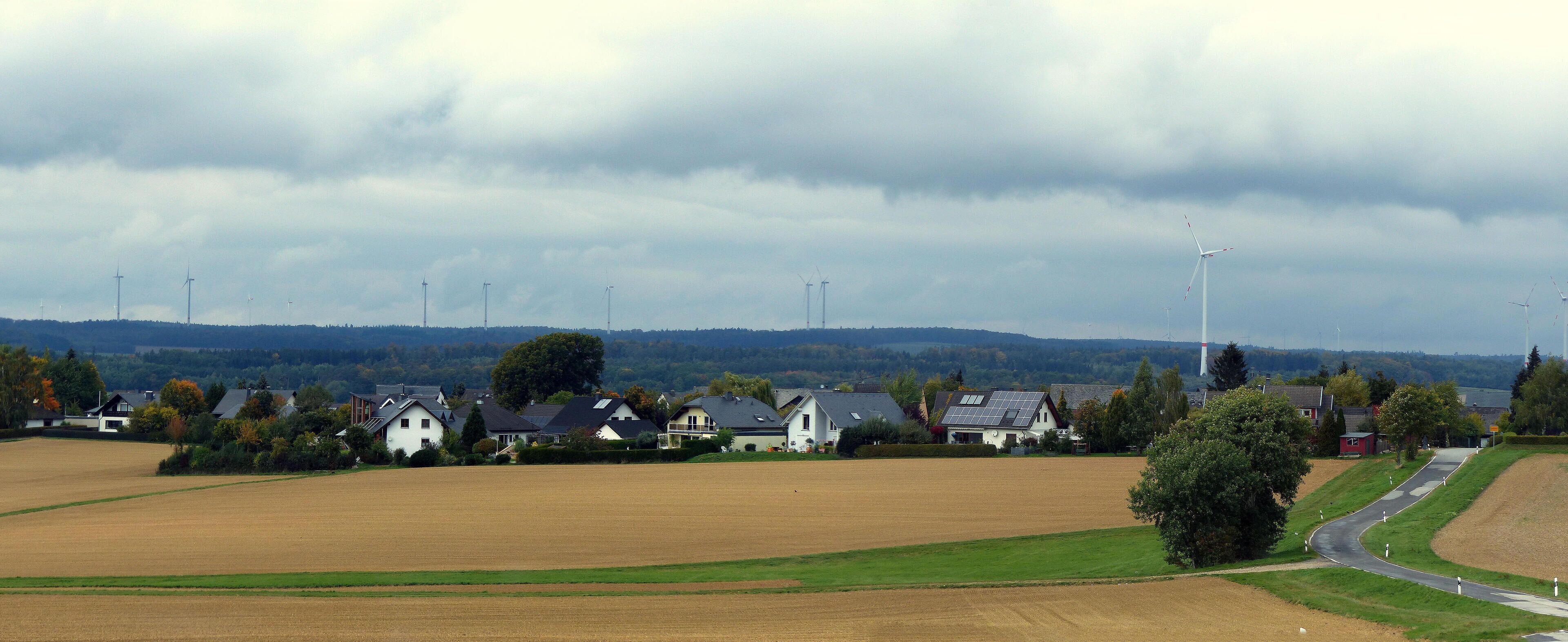 A rural landscape with wind turbines, houses, and fields.