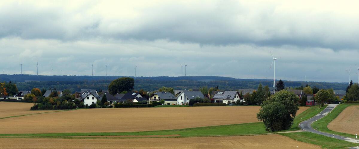 A rural landscape with wind turbines, houses, and fields.