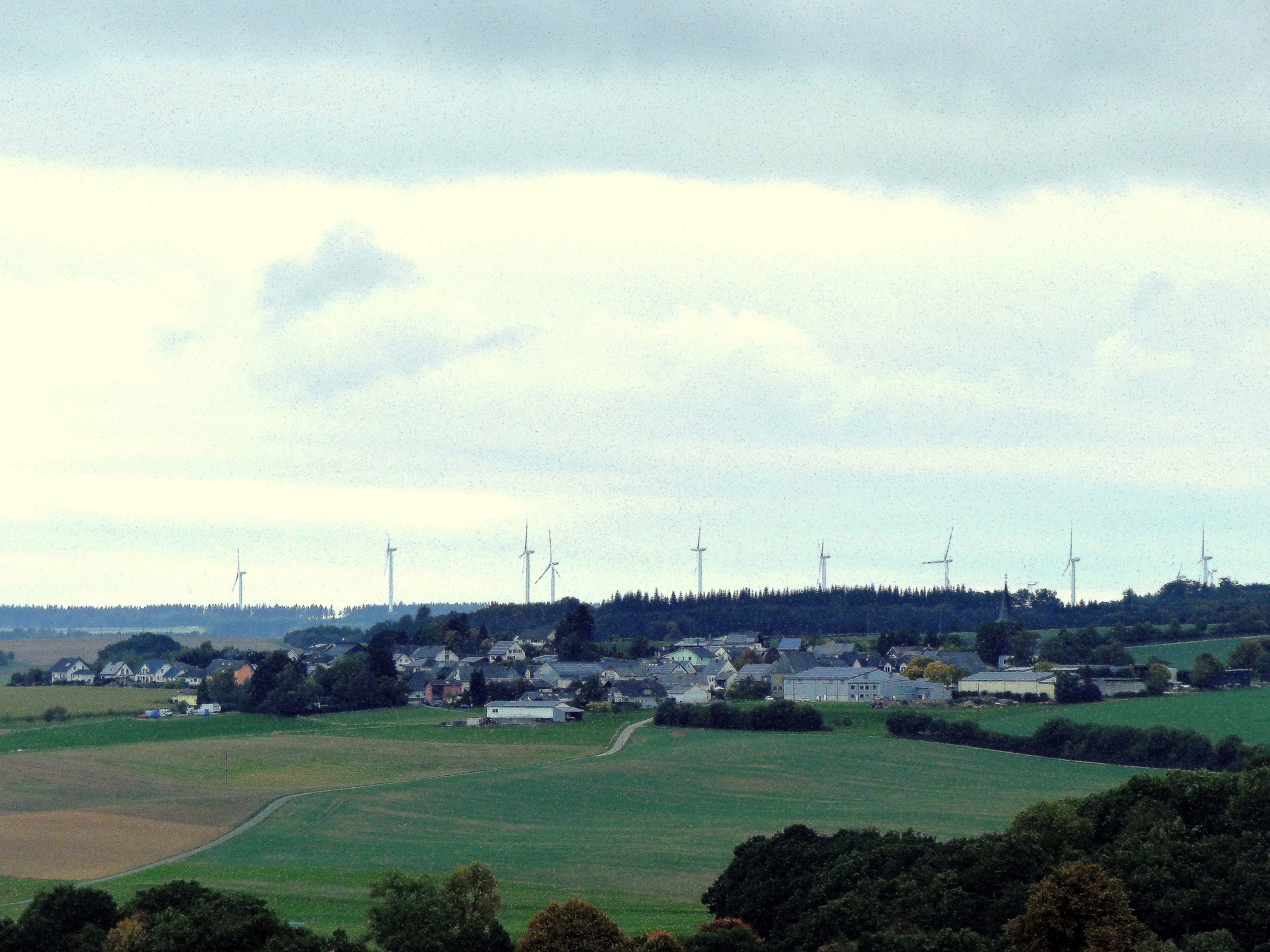 A rural landscape with wind turbines, houses, and fields.