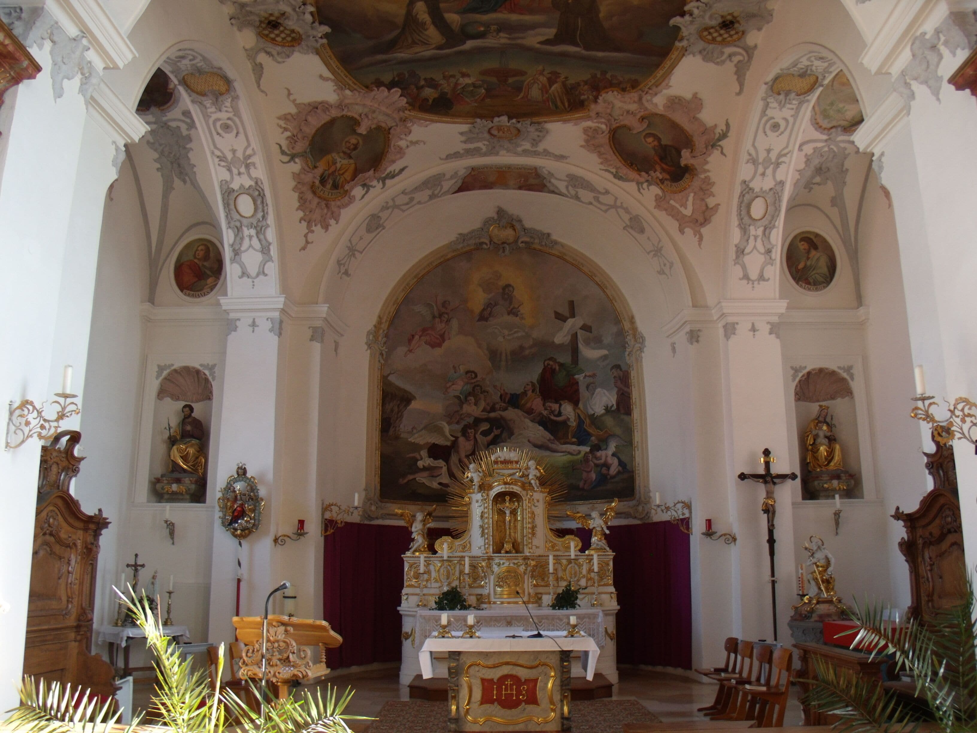 An ornate church interior with a large mural, golden altar, and religious statues.