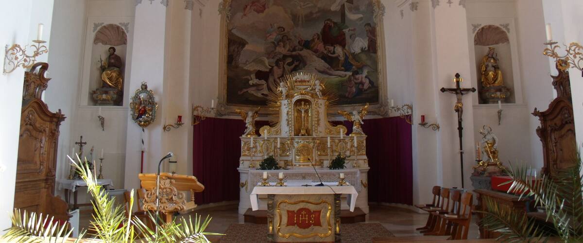 An ornate church interior with a large mural, golden altar, and religious statues.