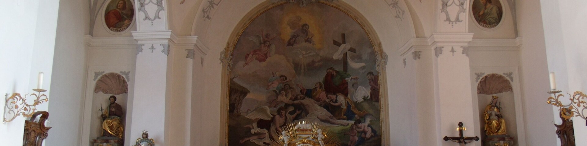 An ornate church interior with a large mural, golden altar, and religious statues.