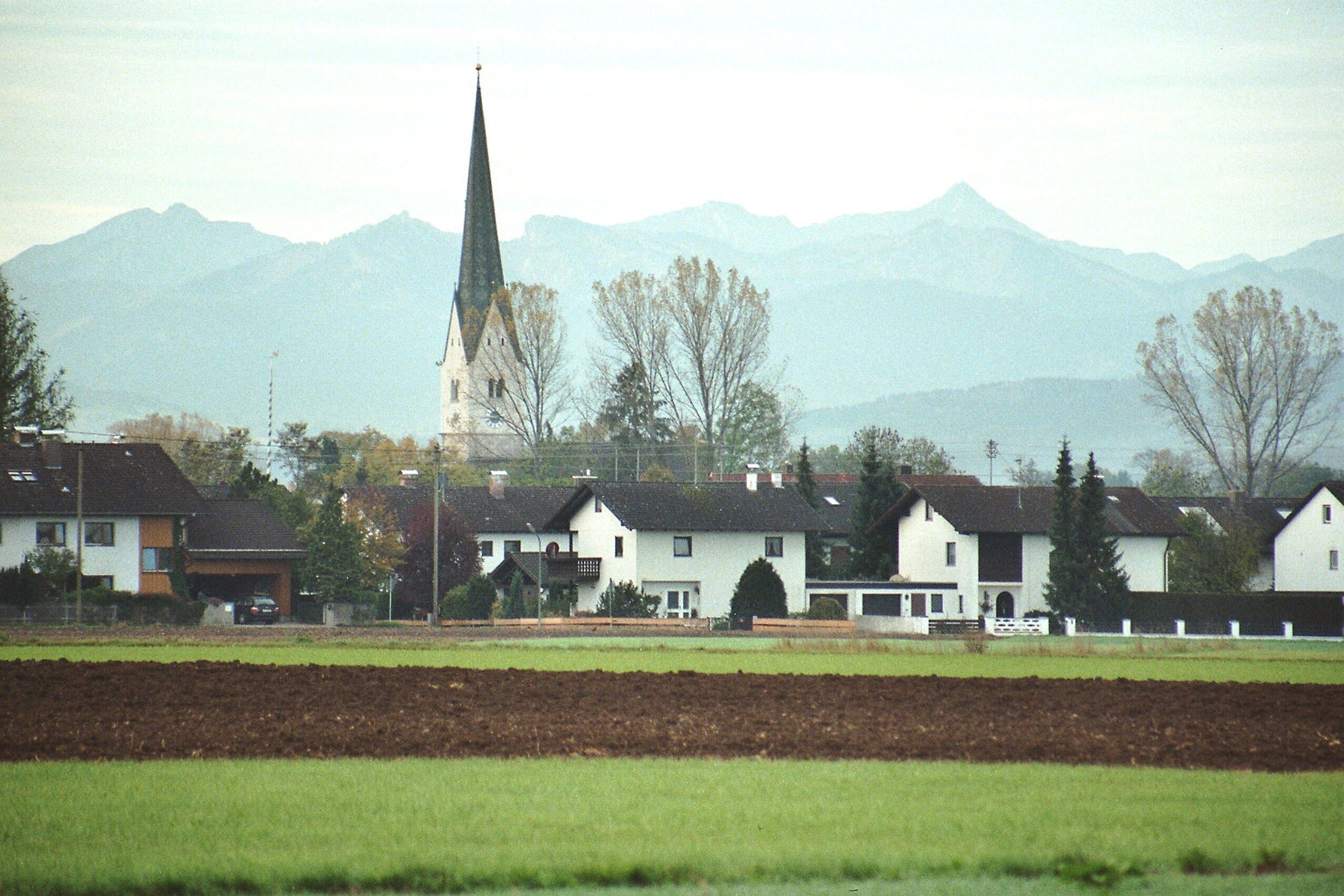 A town with white houses, a church with a tall steeple, and mountains in the background.