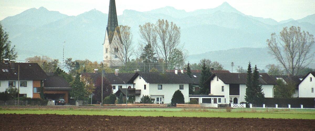 A town with white houses, a church with a tall steeple, and mountains in the background.