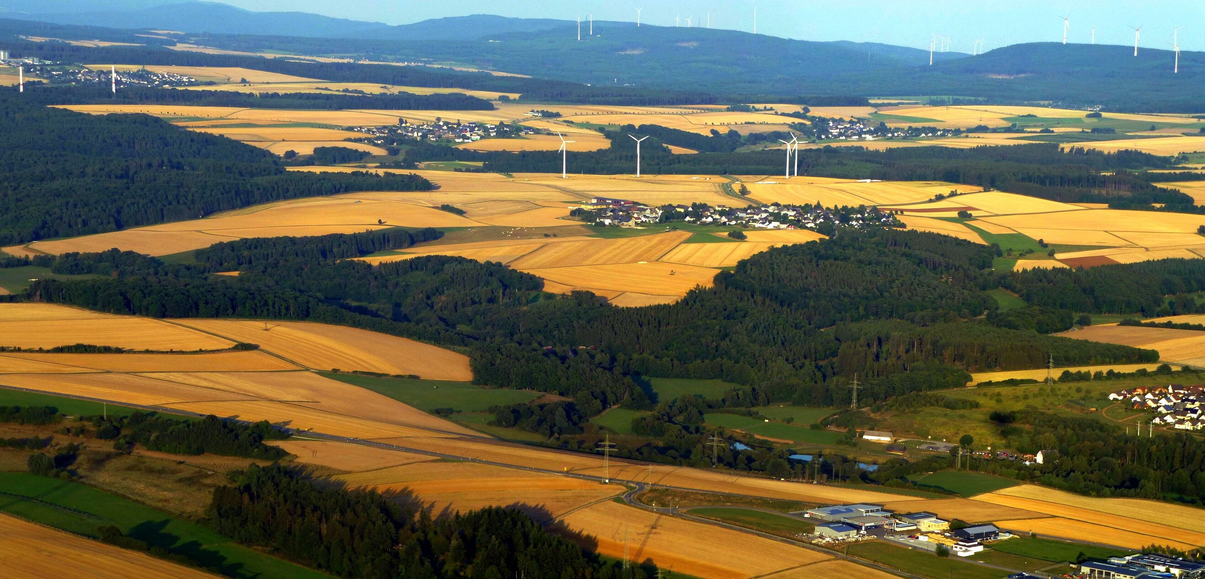 A rural landscape with wind turbines, fields, and a small village.