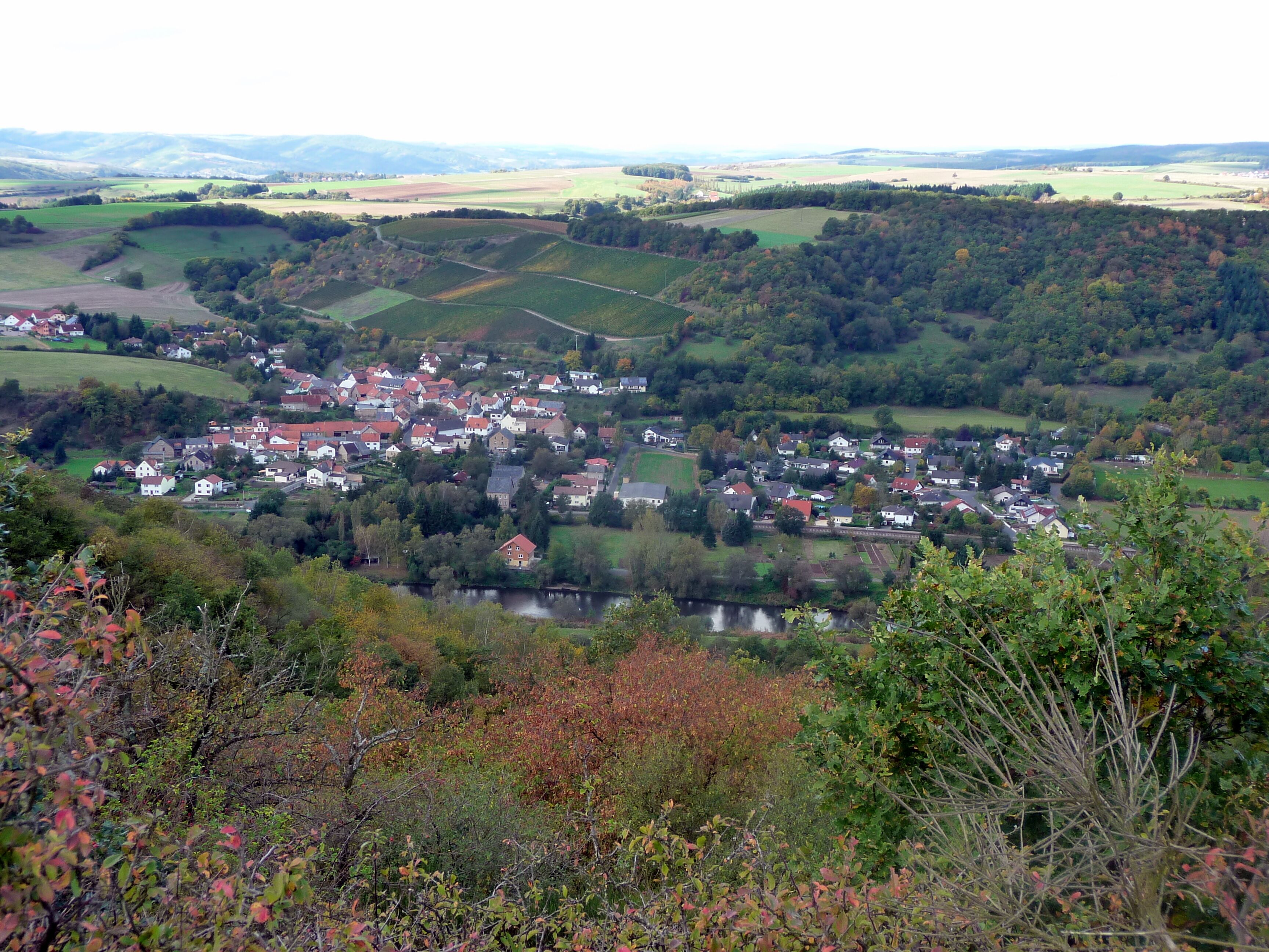 A village nestled in a valley with a river, surrounded by rolling hills and fields.
