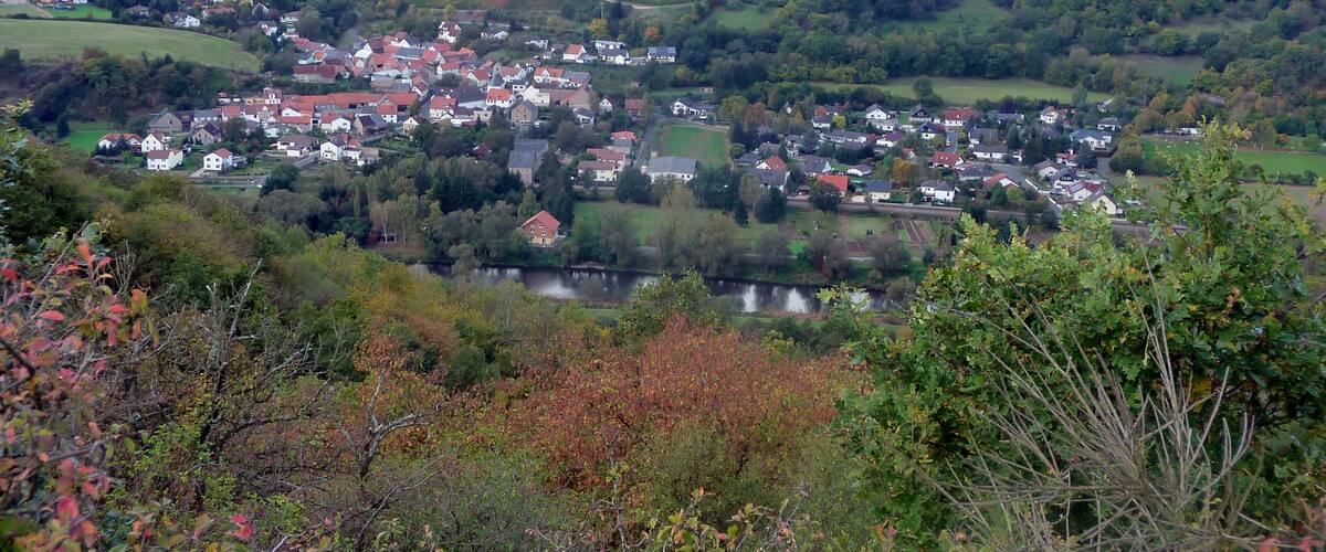 A village nestled in a valley with a river, surrounded by rolling hills and fields.