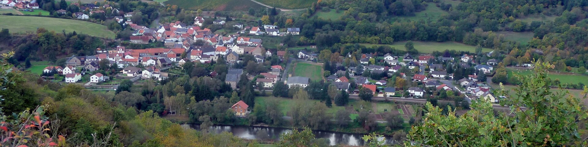 A village nestled in a valley with a river, surrounded by rolling hills and fields.