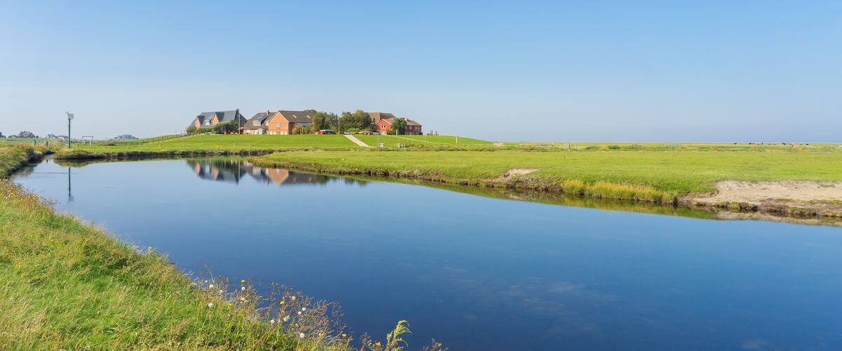 A calm river reflecting houses and a clear blue sky.