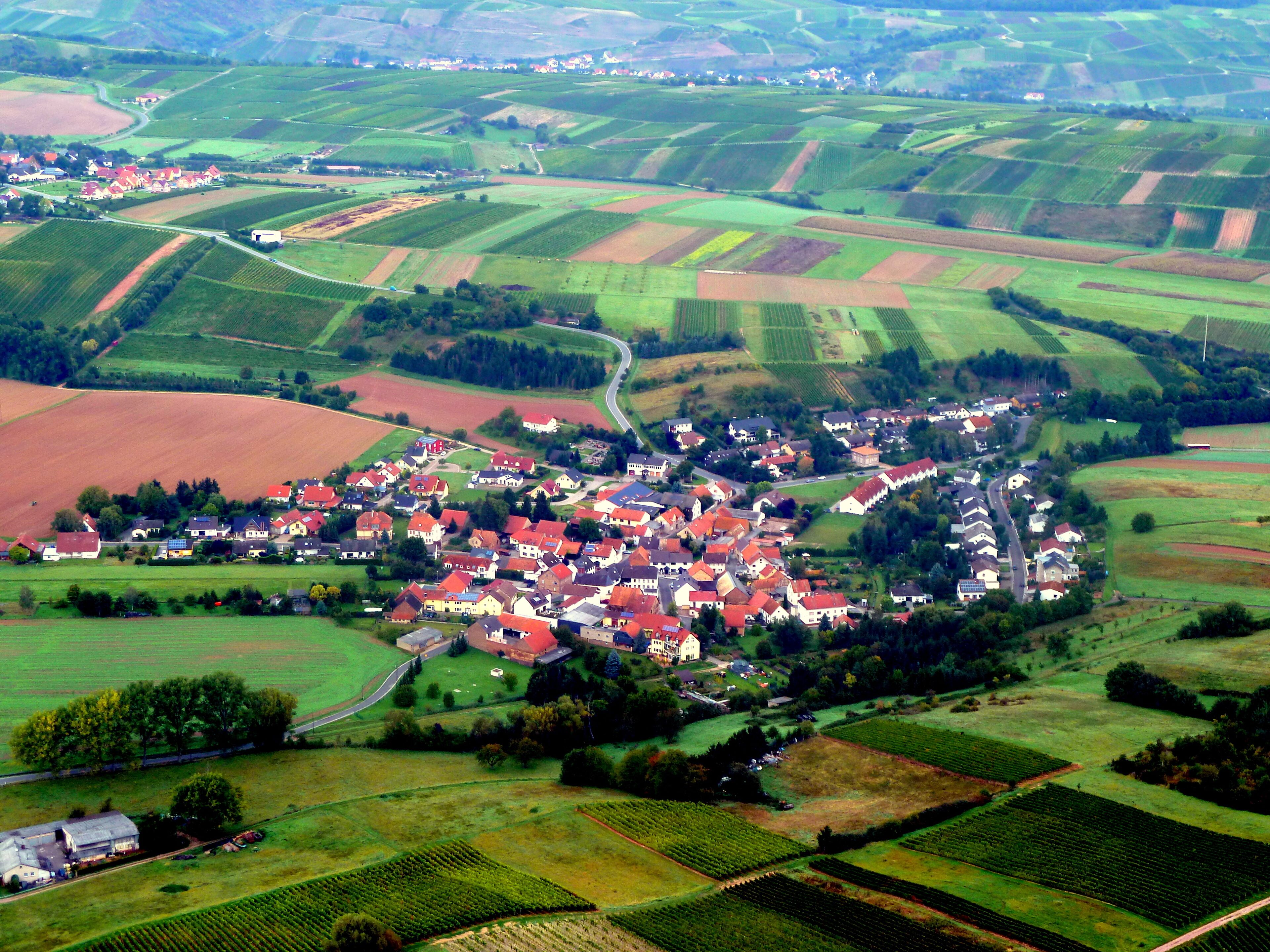 A rural village with red-roofed houses surrounded by green fields and rolling hills.