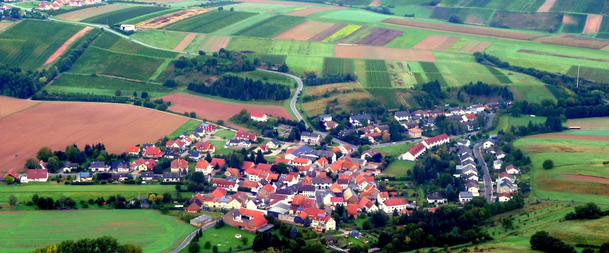 A rural village with red-roofed houses surrounded by green fields and rolling hills.