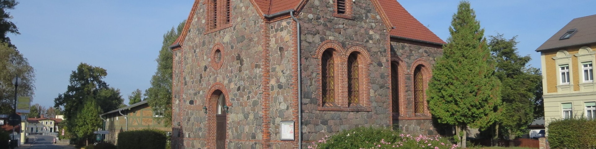 Una iglesia de piedra con techo rojo y ventanas de arco.