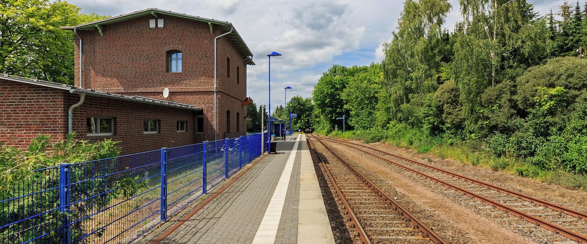 A train station platform with a brick building, blue fencing, and railway tracks.
