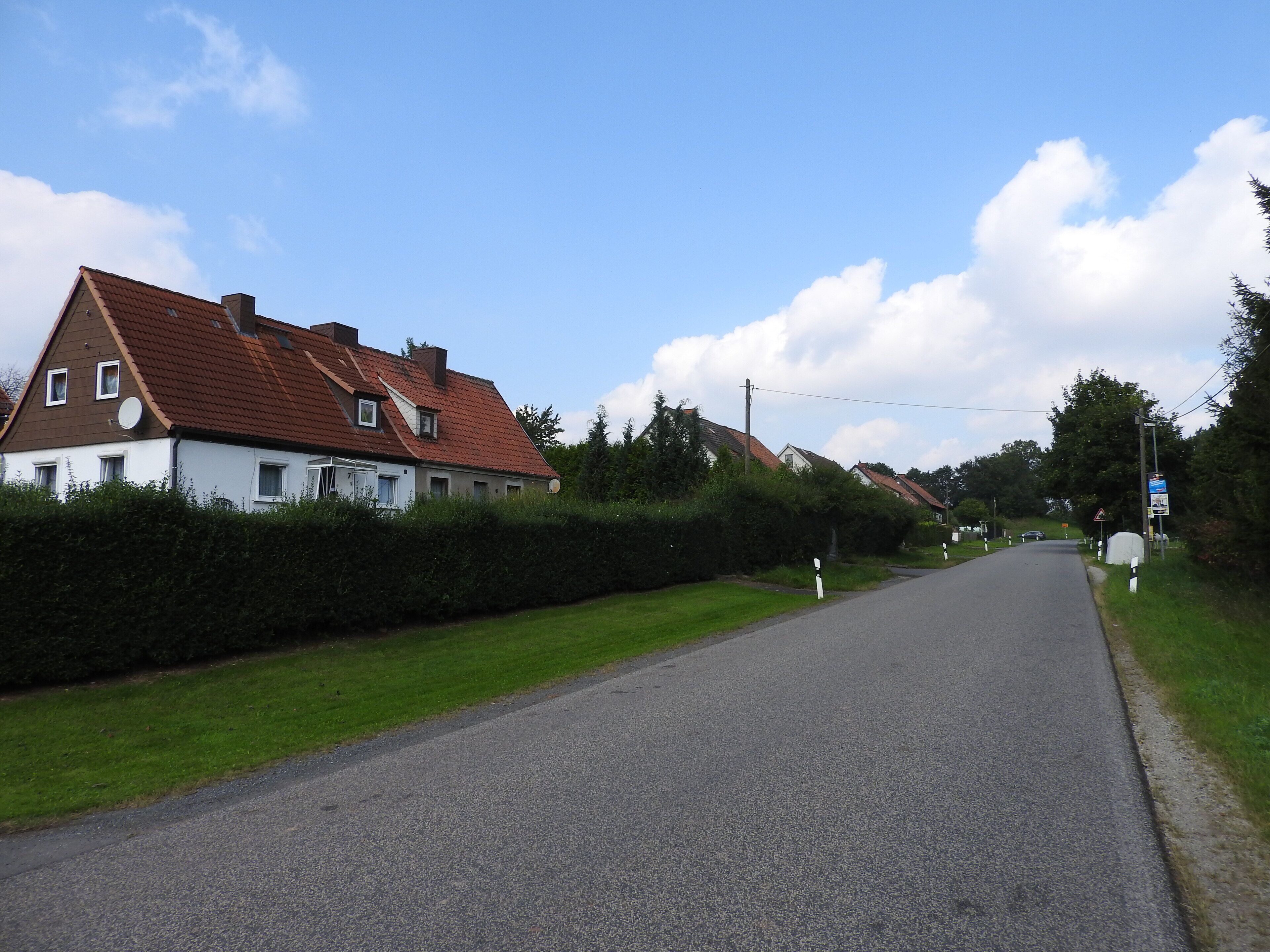 A rural road with houses on one side and a grassy area on the other.