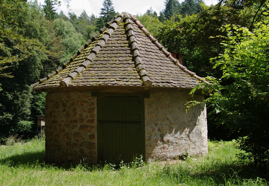 A small stone building with a tiled roof surrounded by lush greenery.
