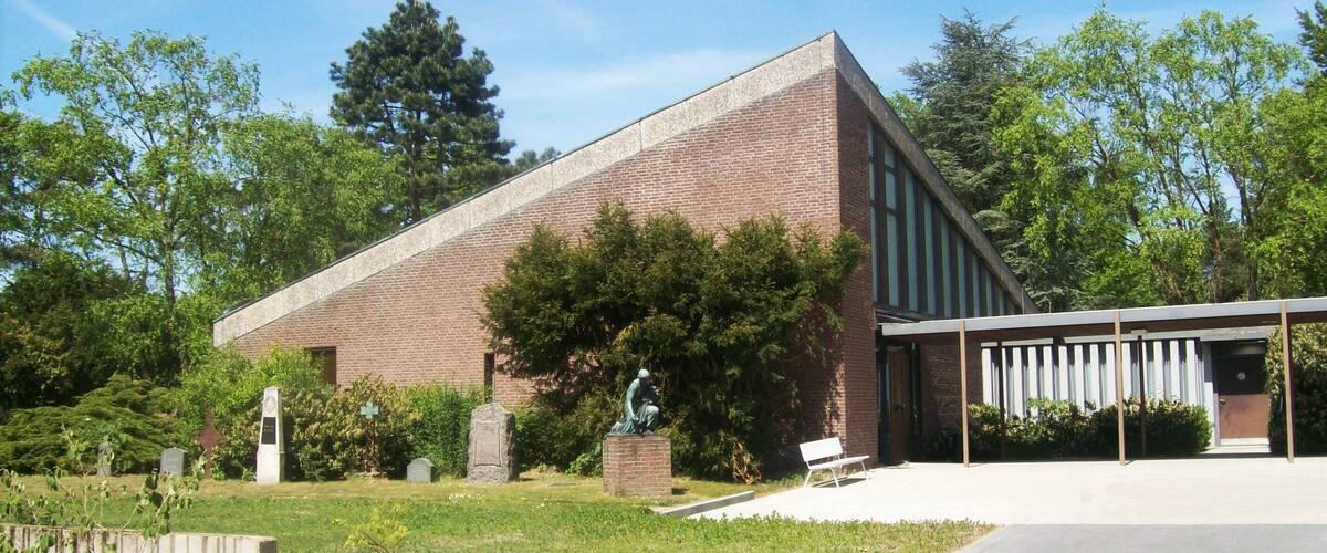 A brick building with a sloped roof, a covered walkway, and a statue in front.