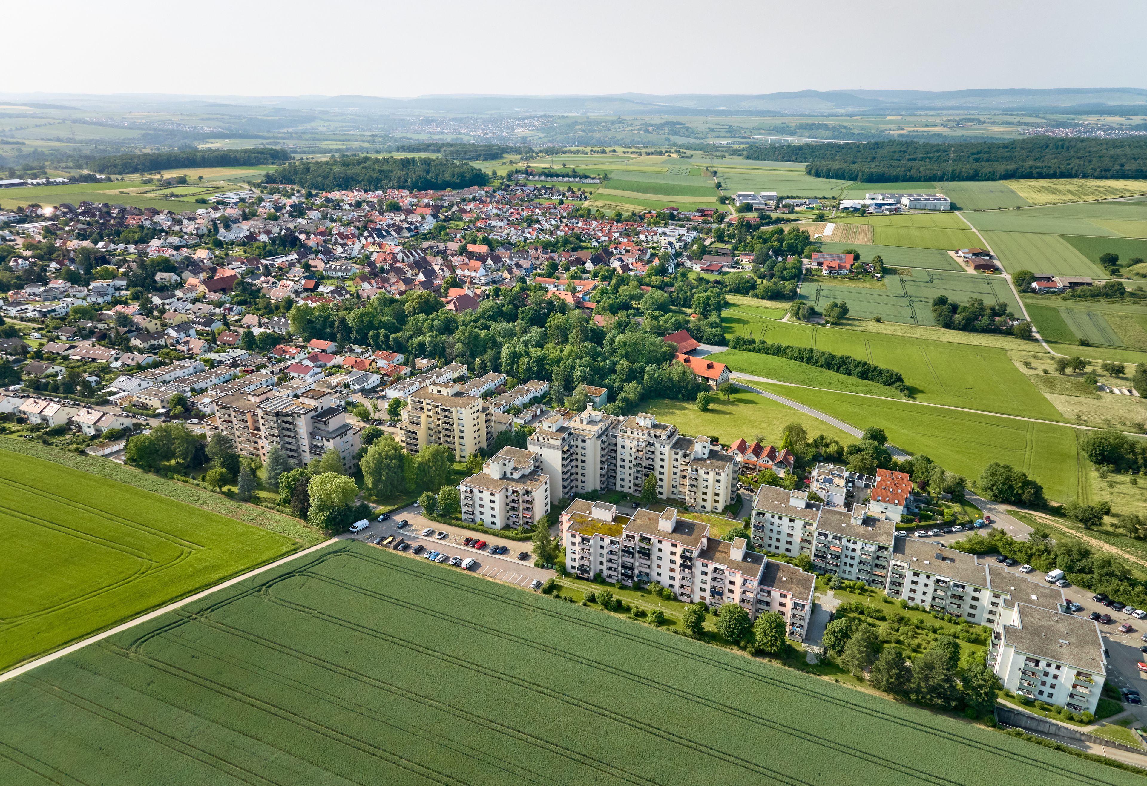 An aerial view of a town with residential buildings, green fields, and a distant bridge.