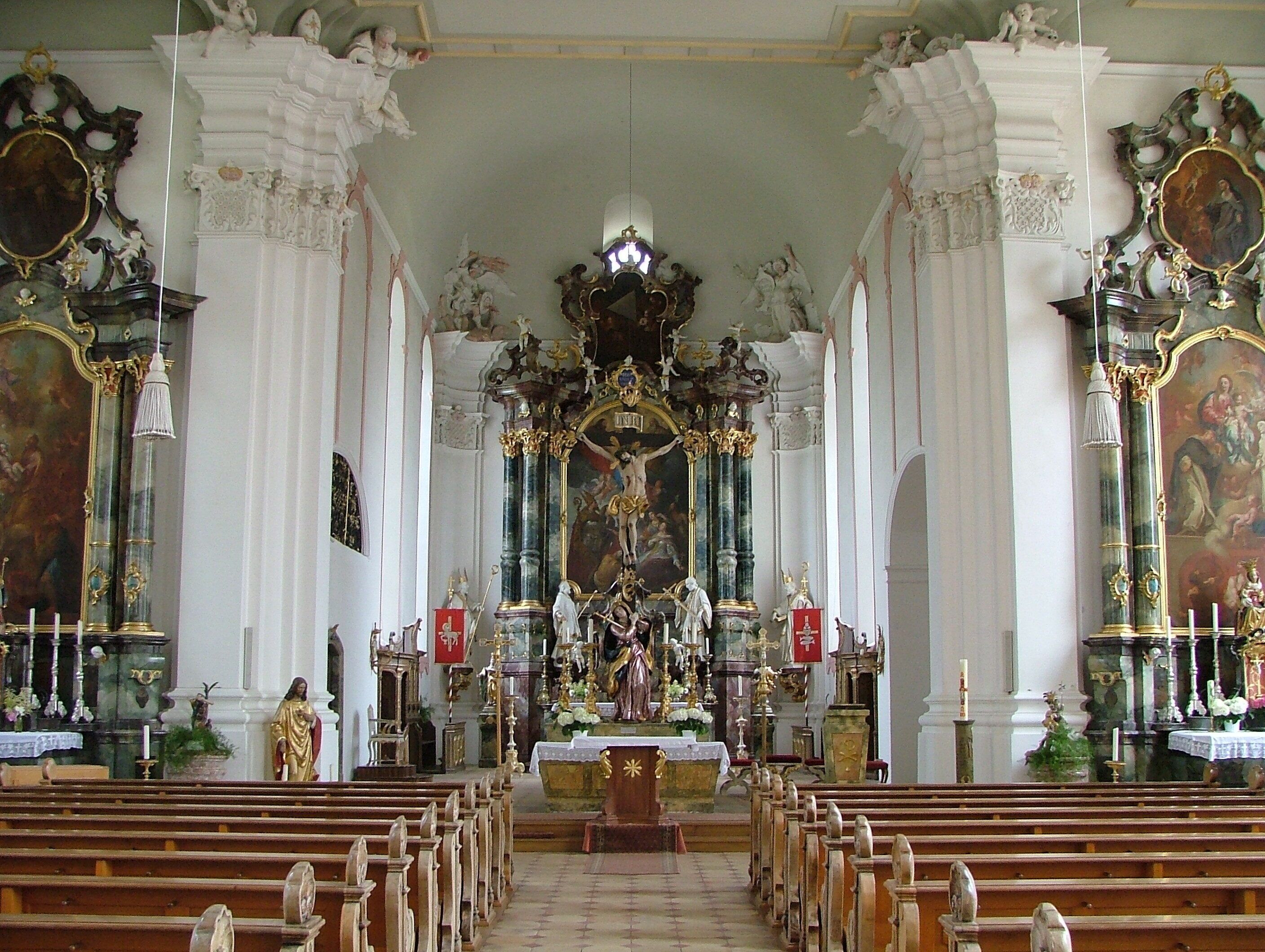 An ornate church interior with rows of wooden pews, a central altar, and elaborate wall decorations.