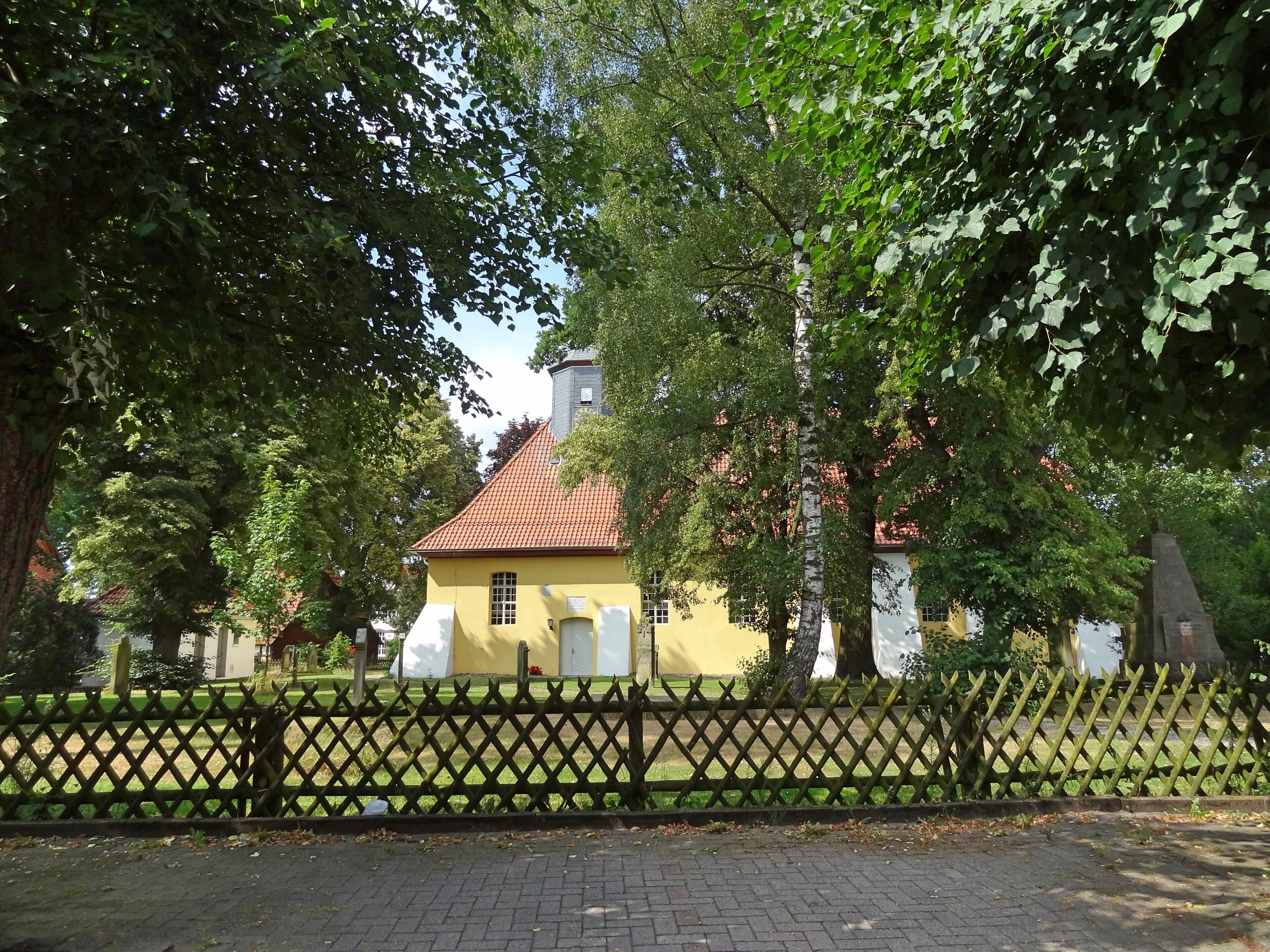 A yellow building with a red roof, surrounded by a wooden fence and trees.