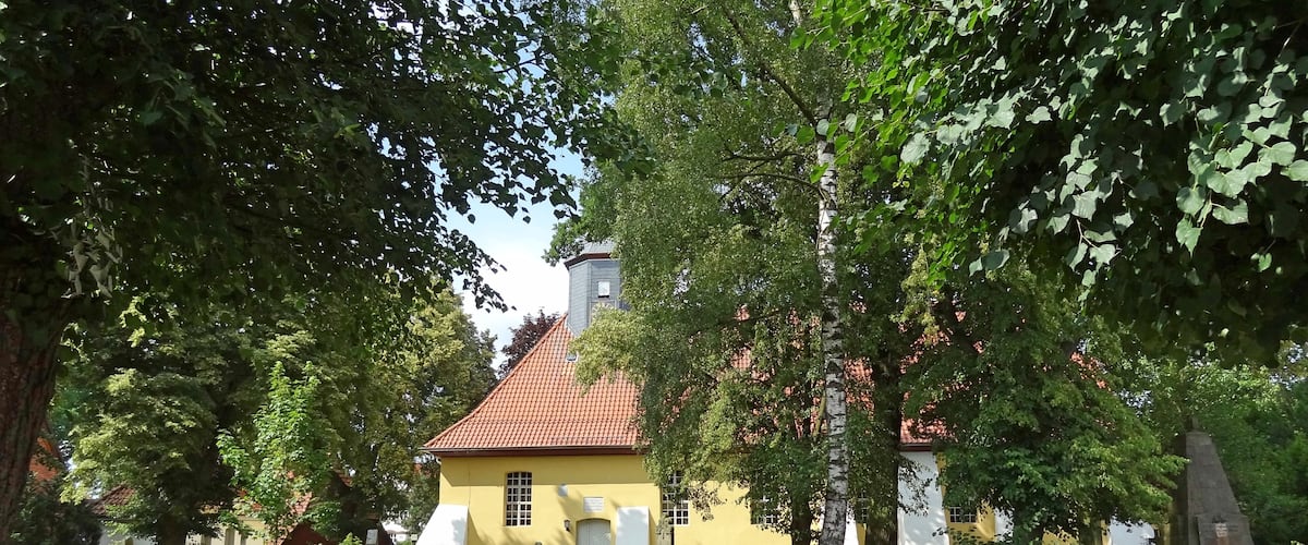 A yellow building with a red roof, surrounded by a wooden fence and trees.