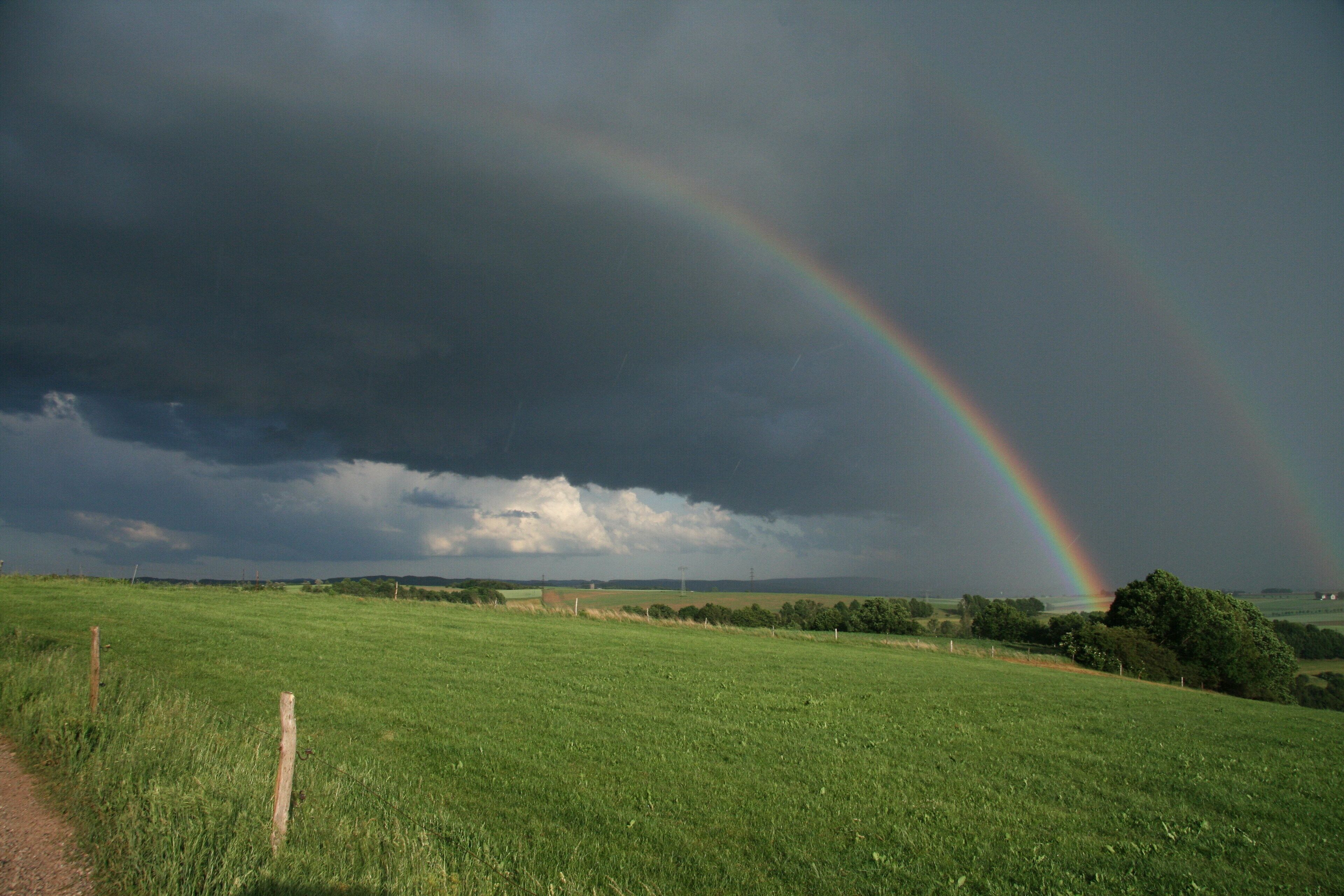 A green field with a rainbow and stormy sky.