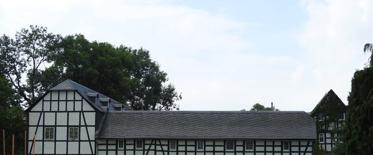 A traditional half-timbered house with a sloped roof, surrounded by a grassy field and trees.