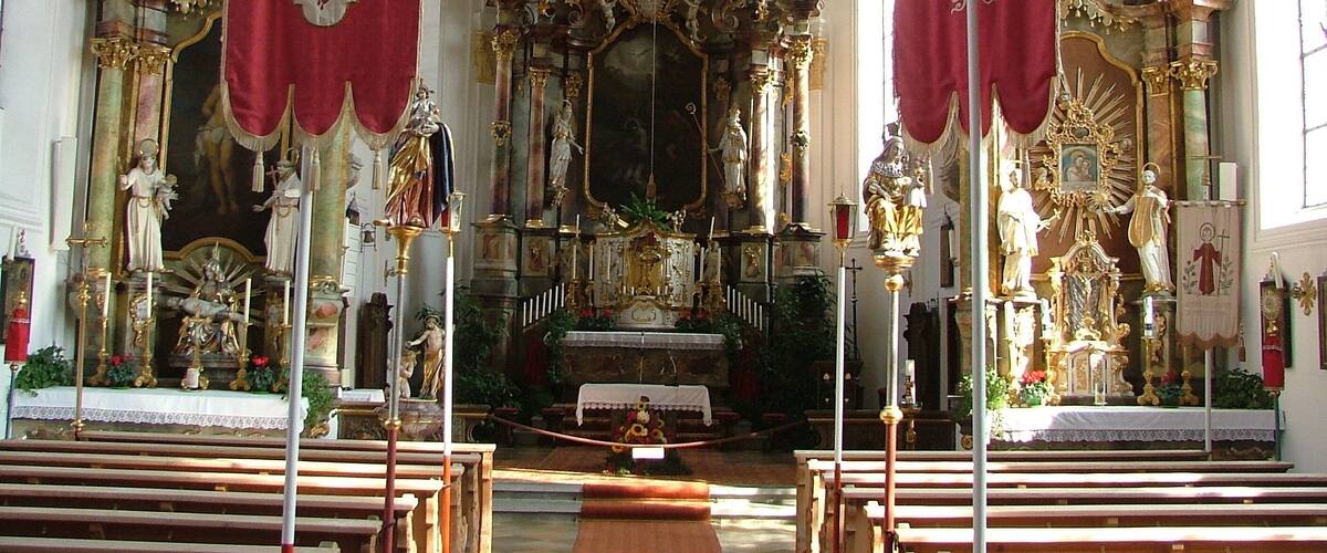 An ornate church interior with red banners, golden statues, and a central altar.
