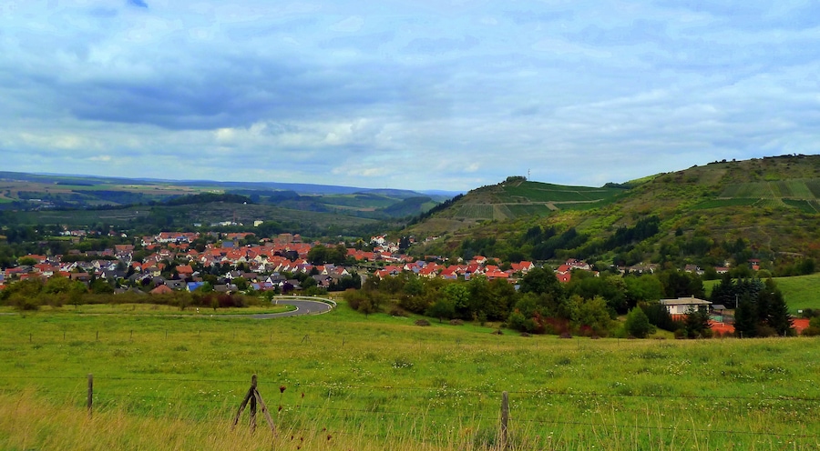 A rural village with red-roofed houses surrounded by green fields and rolling hills.