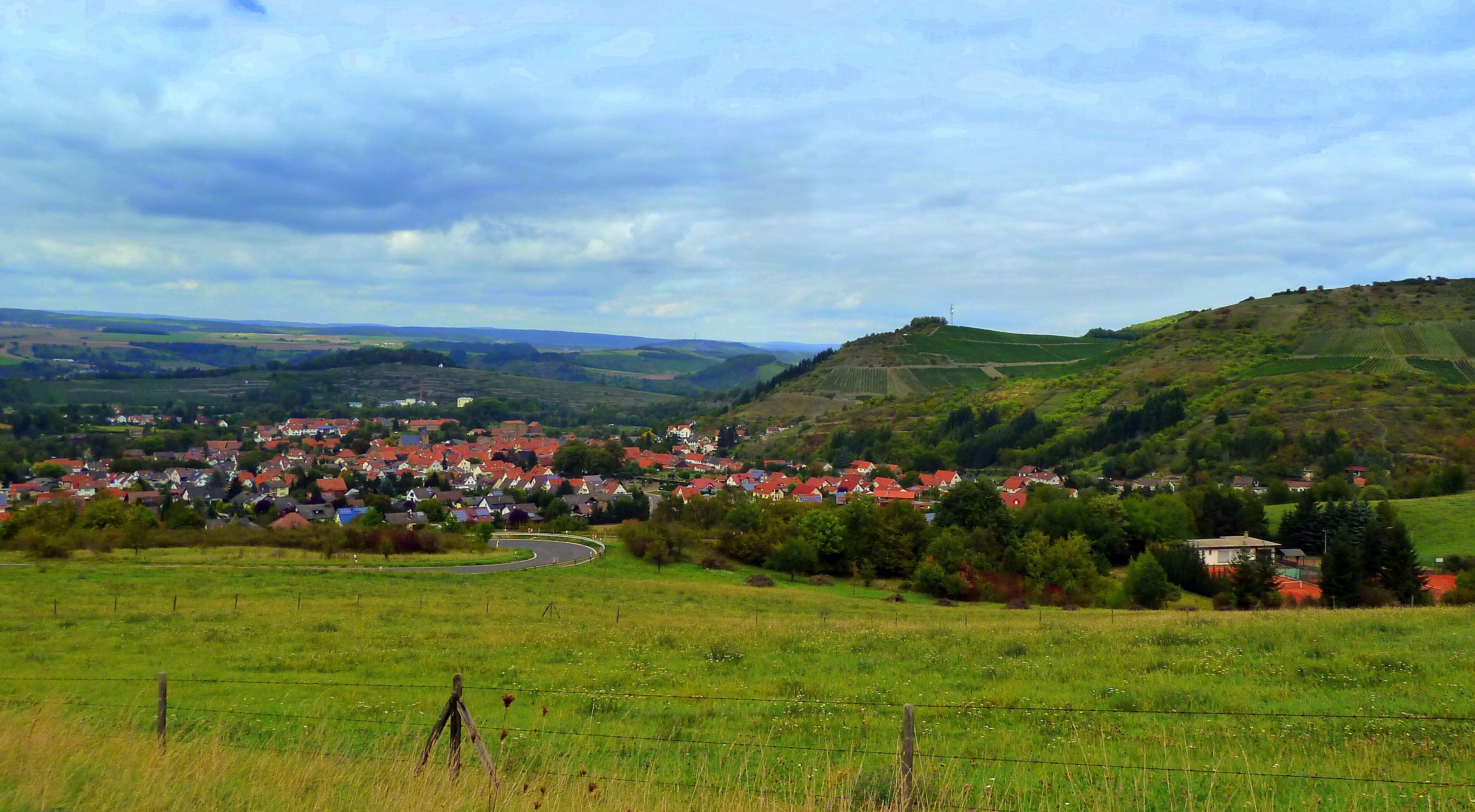 A rural village with red-roofed houses surrounded by green fields and rolling hills.