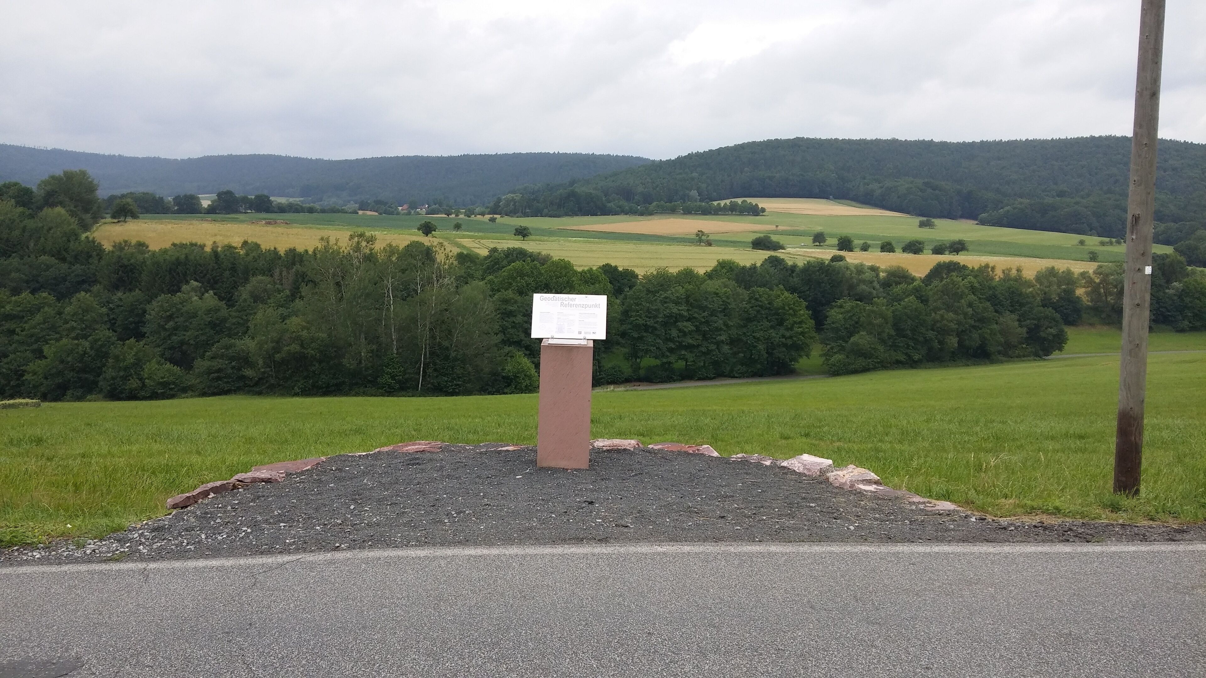 A rural landscape with a signpost in the foreground and a hilly background.