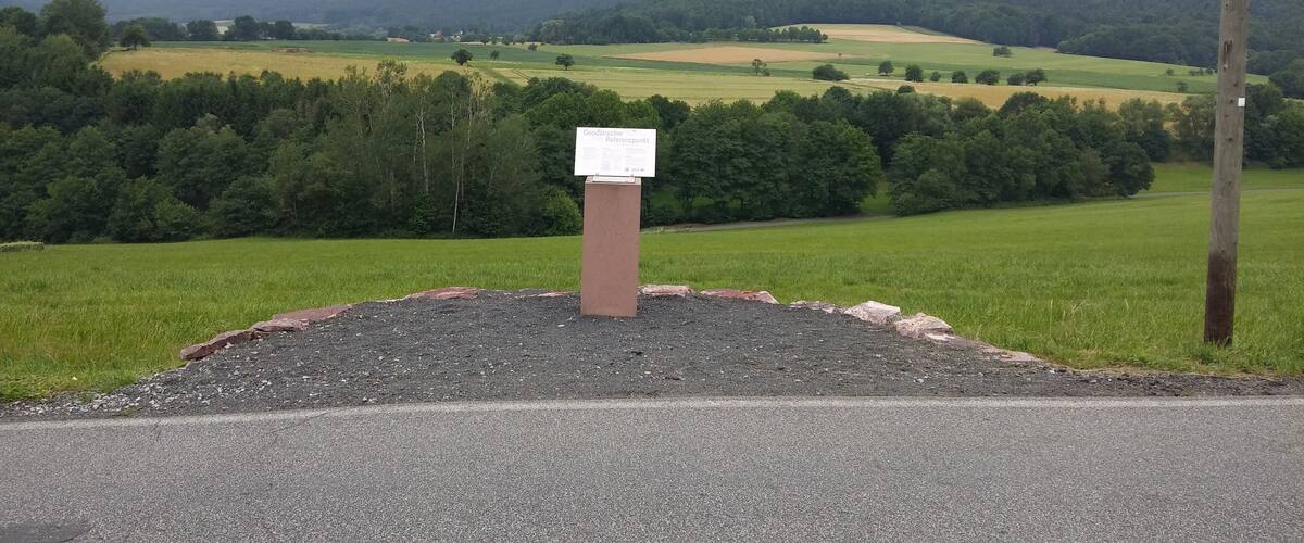 A rural landscape with a signpost in the foreground and a hilly background.