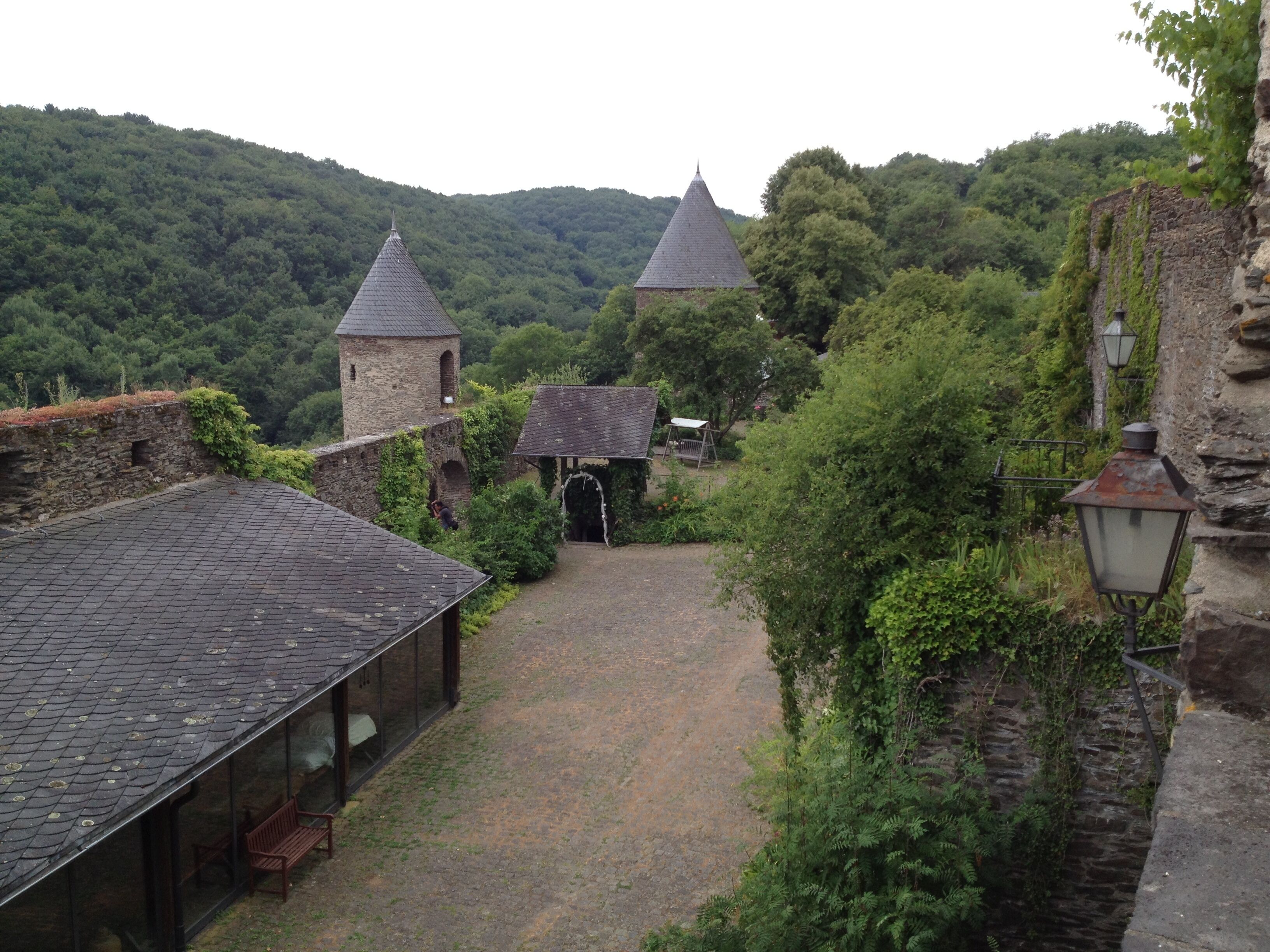 A historic stone building with a conical roof, surrounded by lush greenery and a cobblestone path.