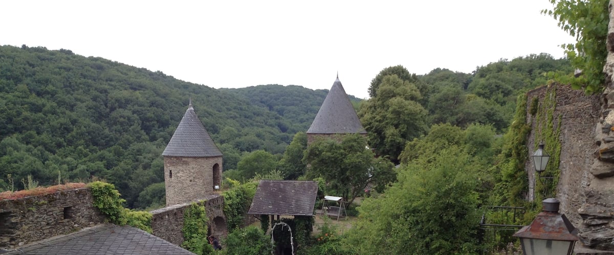 A historic stone building with a conical roof, surrounded by lush greenery and a cobblestone path.