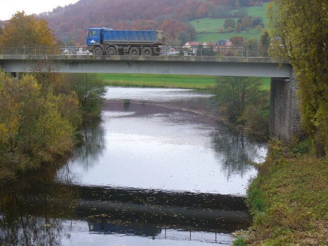 A blue truck crossing a bridge over a river with surrounding greenery.