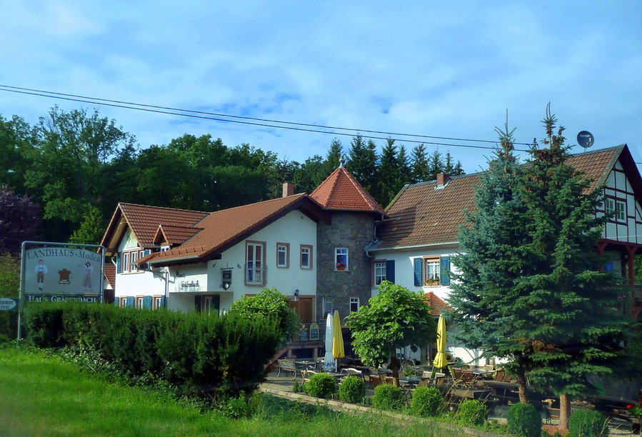 A traditional European building with a signboard, surrounded by lush greenery and trees.