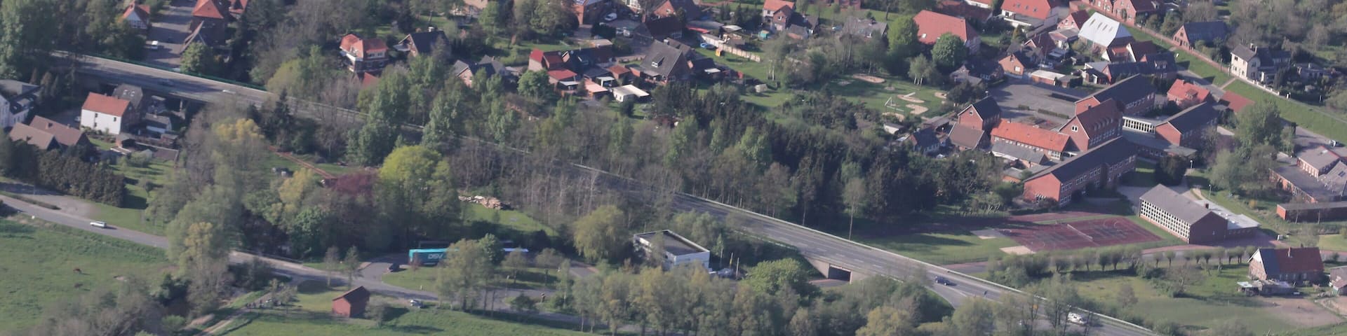 An aerial view of a rural village with red-roofed houses, green fields, and a river.